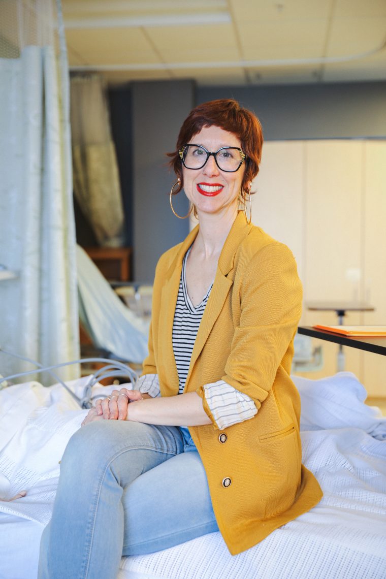 Christina Hart smiles while seated on a hospital bed in a nursing simulation lab classroom.