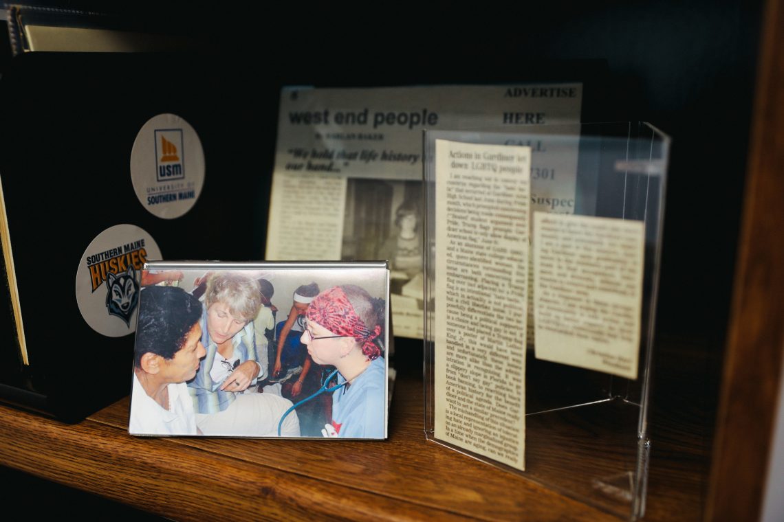 Shelf in Christina Hart’s office displaying a photo of her providing care in the Dominican Republic alongside newspaper clippings highlighting her work and research.