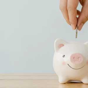 Hand placing a coin into a small piggy bank on a wooden surface.