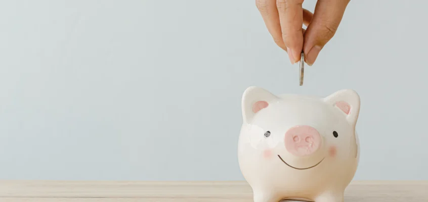 Hand placing a coin into a small piggy bank on a wooden surface.