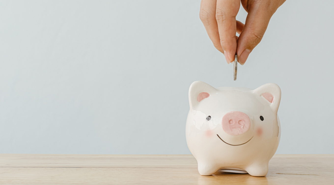 Hand placing a coin into a small piggy bank on a wooden surface.