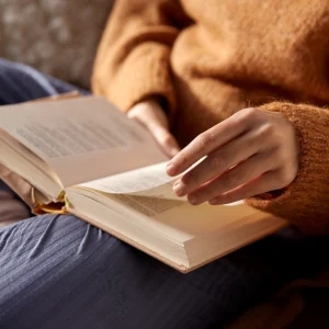 Person sitting on a couch flipping through the pages of a book.