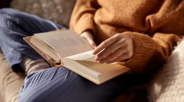 Person sitting on a couch flipping through the pages of a book.