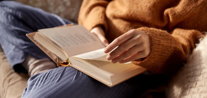 Person sitting on a couch flipping through the pages of a book.