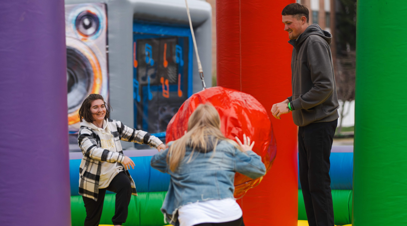 Students play in an inflatable bounce house with a large red ball at spring fling.