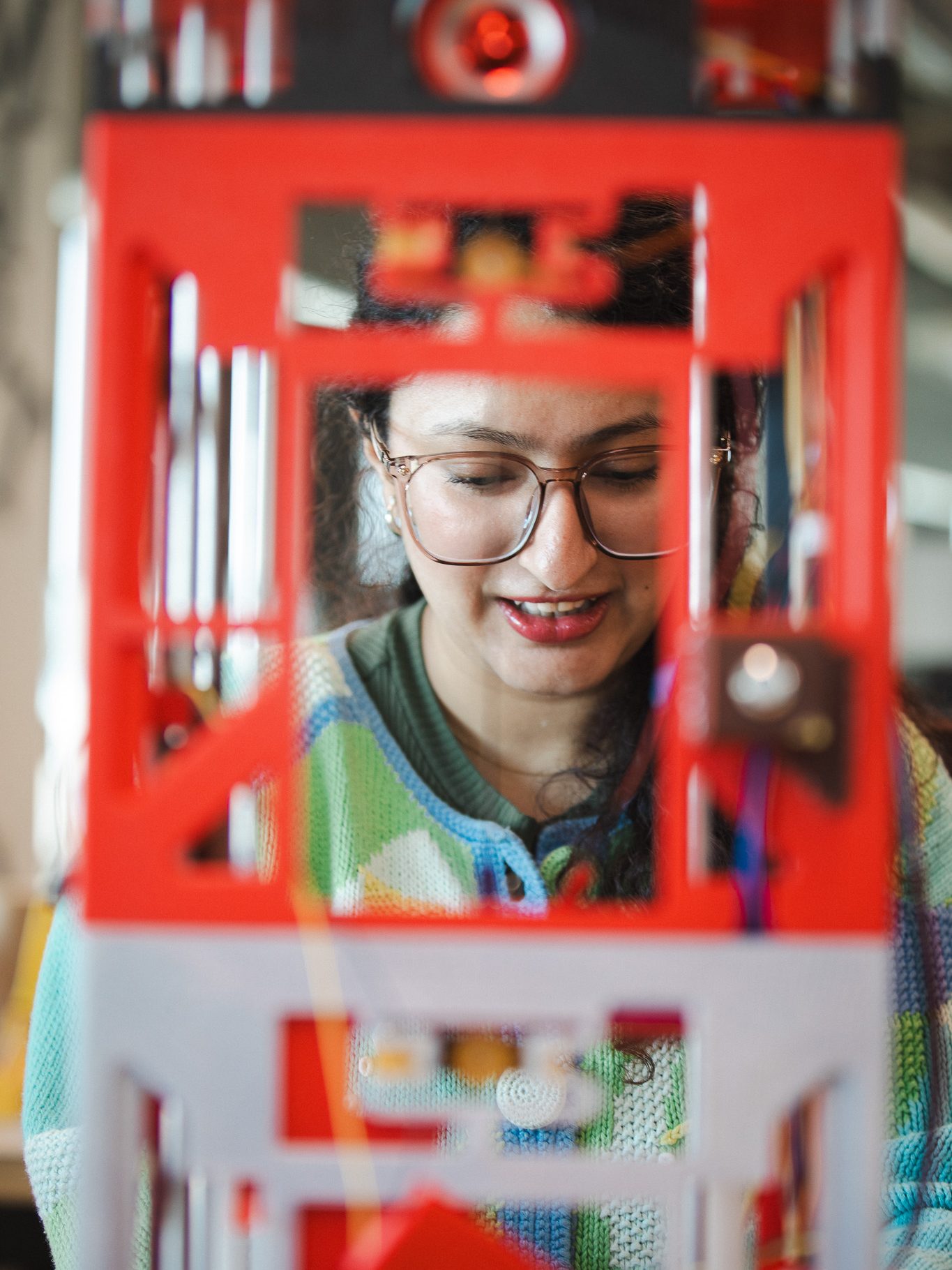Prashiddhi Pokhrel smiles, seen through the latticed structure of a 3D printed elevator model in USM's Maker Innovation Studio.