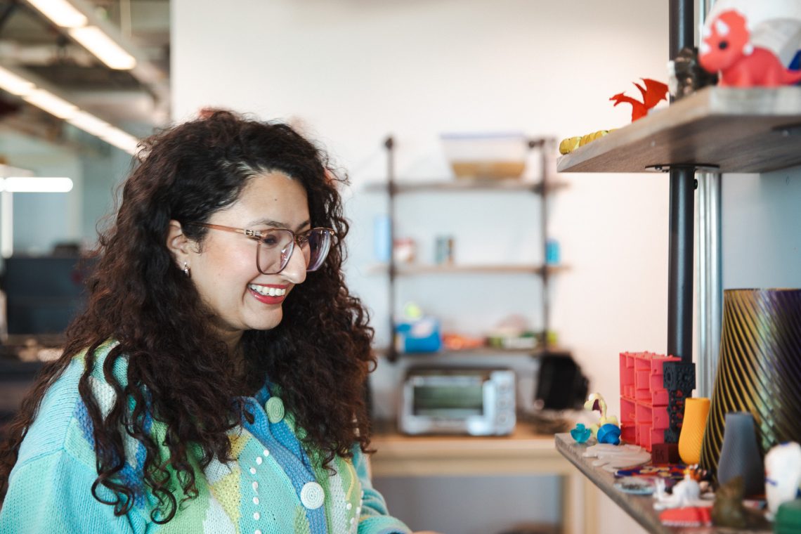Prashiddhi Pokhrel, in profile, laughs as she shows off a collection of 3D printed objects in the MIST Lab at the University of Southern Maine.