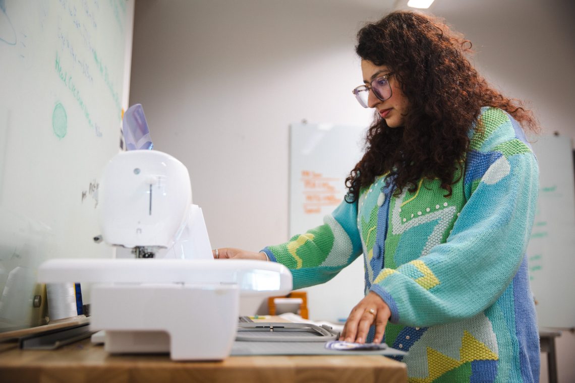 Prashiddhi Pokhrel, in profile, clicks through settings on a digital embroidery machine in the MIST Lab at the University of Southern Maine.
