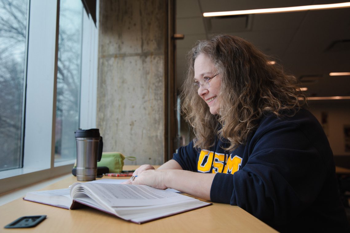 Lisa Struebing writes in a notebook at a desk in the Dubyak Center on USM's Portland campus.