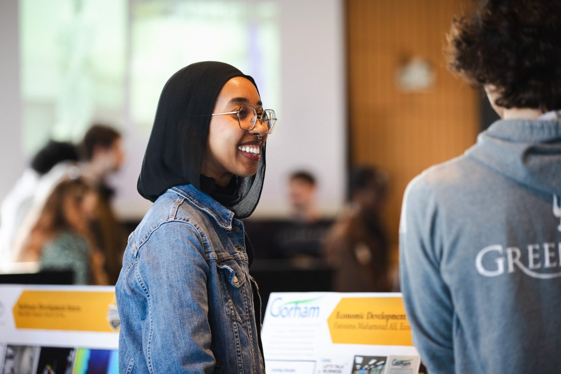 A USM student smiles while speaking with another student at a career or internship fair, with employer and organization displays visible in the background. A USM student smiles while speaking with another student at a career or internship fair, with employer and organization displays visible in the background.