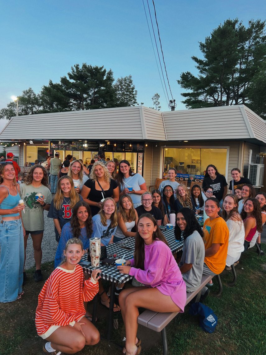 A group of students smile together at an ice cream shop, some holding ice cream.