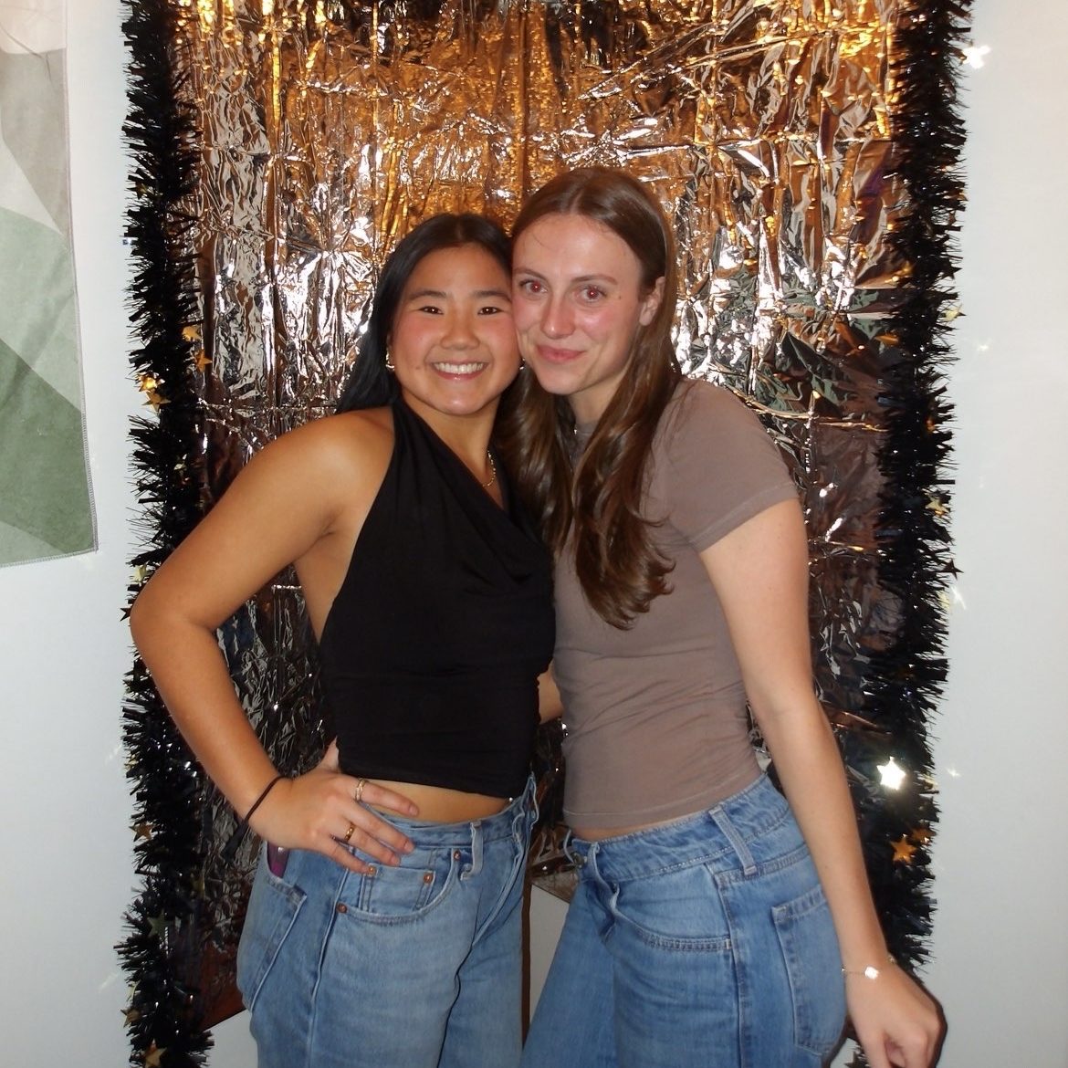 USM student writer Bridgette Toland and sophomore Ani Roberts smile together in front of a metallic backdrop.