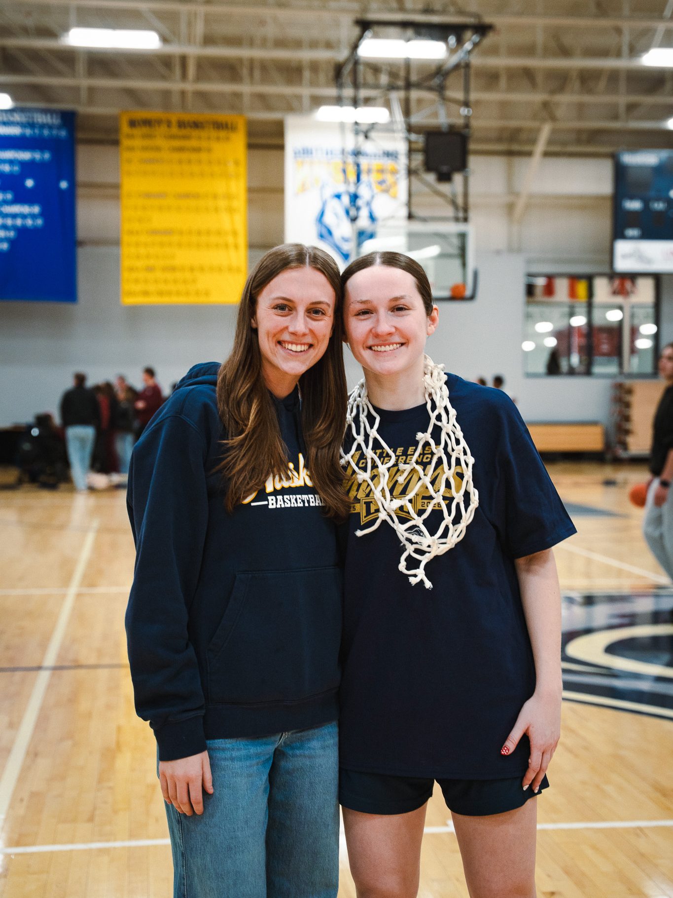 Two students, including author, smile on a basketball court, one wearing a basketball net around her neck.