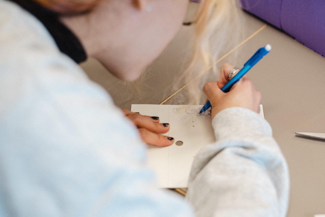 A student writes at the top of a blank notebook page.