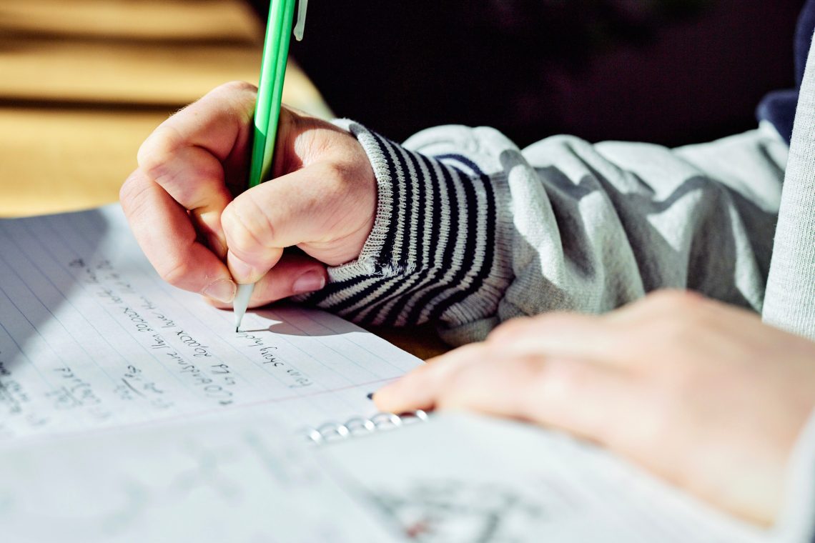 A person writing notes on paper with a mechanical pencil in natural indoor light.