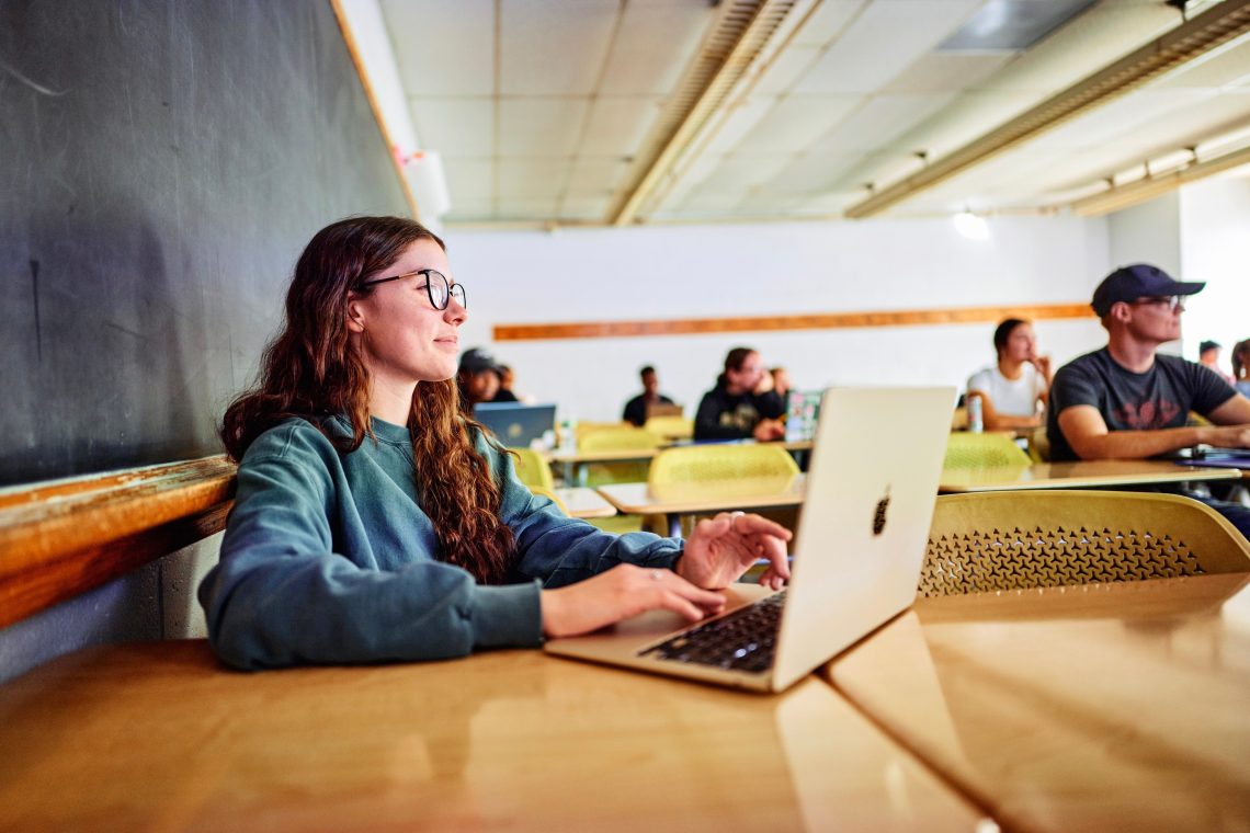 A USM student smiles while working on her laptop in a campus classroom.