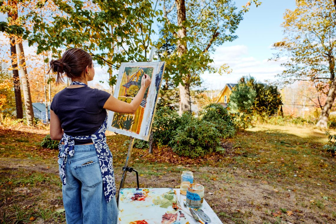 A USM student works on a plein air painting outside, brush in hand.