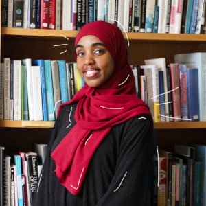 Najmo Ahmed smiles in front of a wall of bookshelves.