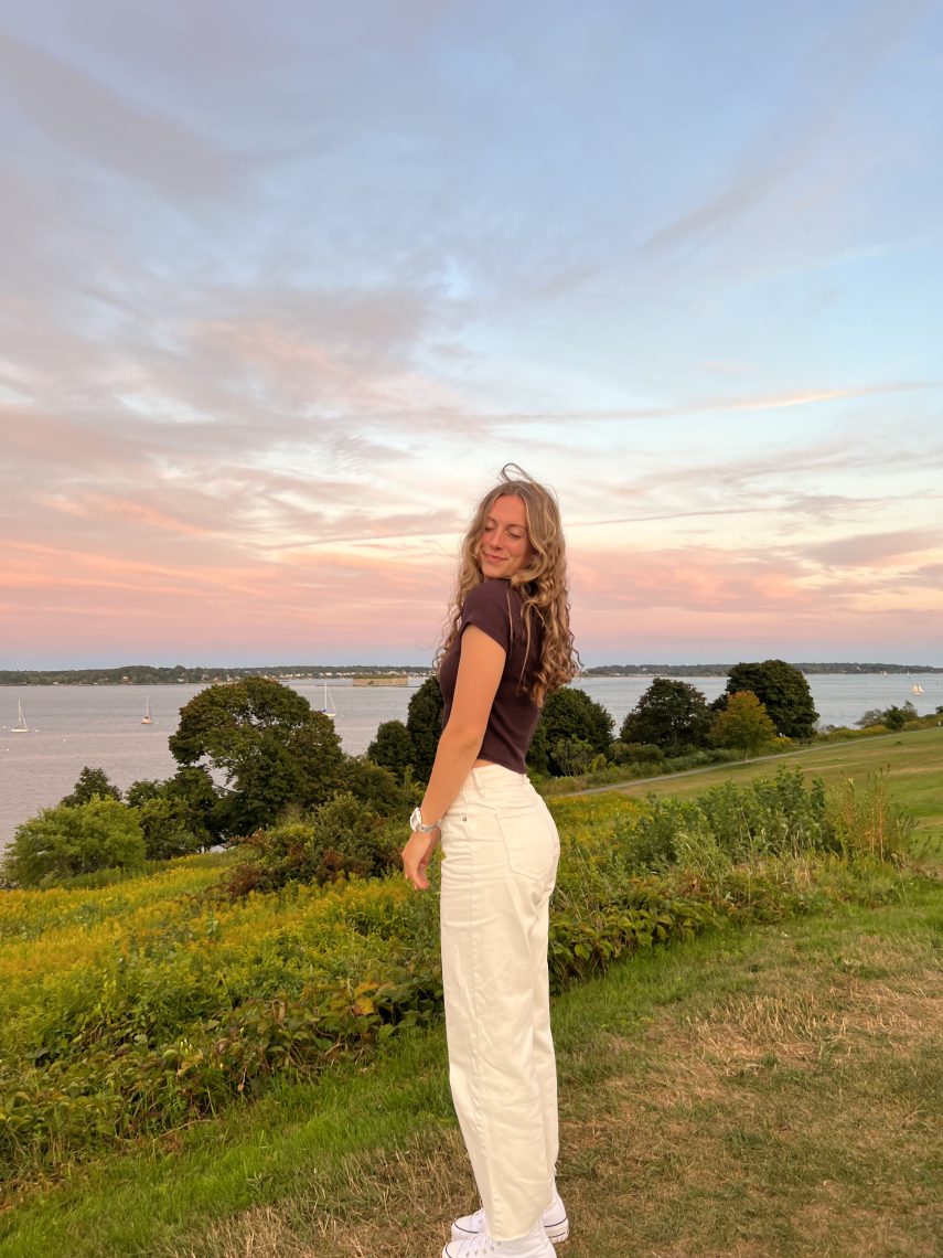 Bridgette, the author, smiling at the camera while standing at the Eastern Promenade at sunset, with the harbor and islands in the background.