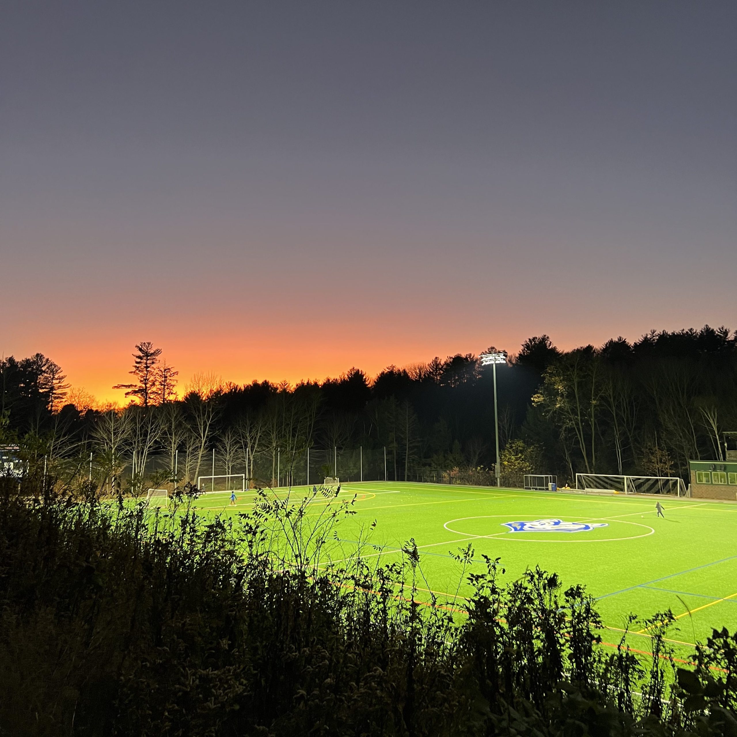Gorham campus soccer field lit up at sunset, with a dark orange sky creating a dramatic backdrop.