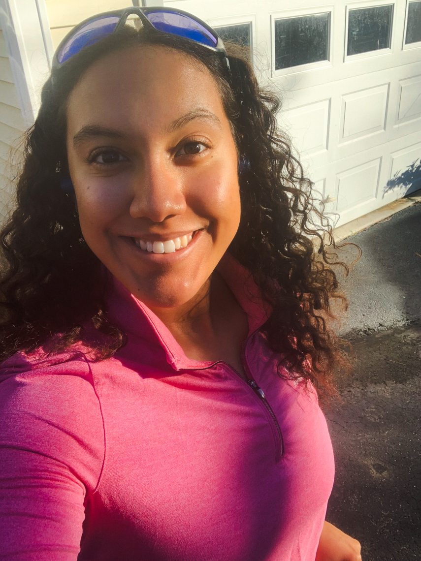 Eliana Tardiff smiles in a pink quarter-zip top with sunglasses pushed up on her head, photographed outdoors in warm afternoon light.