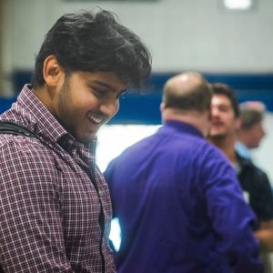 A student smiles while navigating a career fair, with a illustrated briefcase graphic overlaid on the image. A student smiles while navigating a career fair.