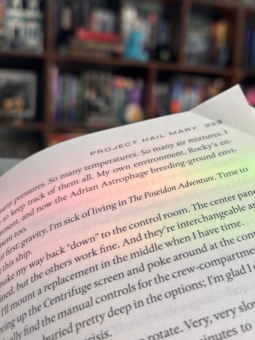 An open copy of "Project Hail Mary" by Andy Weir, showing page 333, held up in front of a blurred bookshelf in the background.