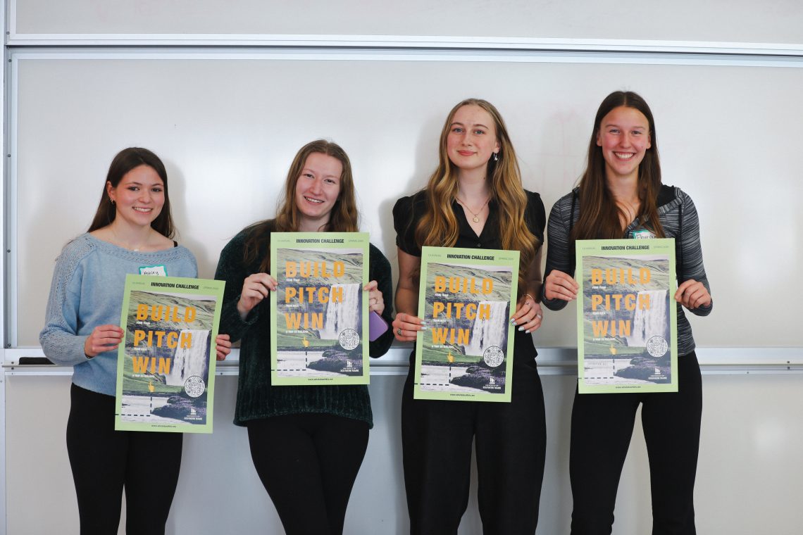 Four smiling students hold What About This? Innovation Challenge posters reading "Build, Pitch, Win" at the kickoff event