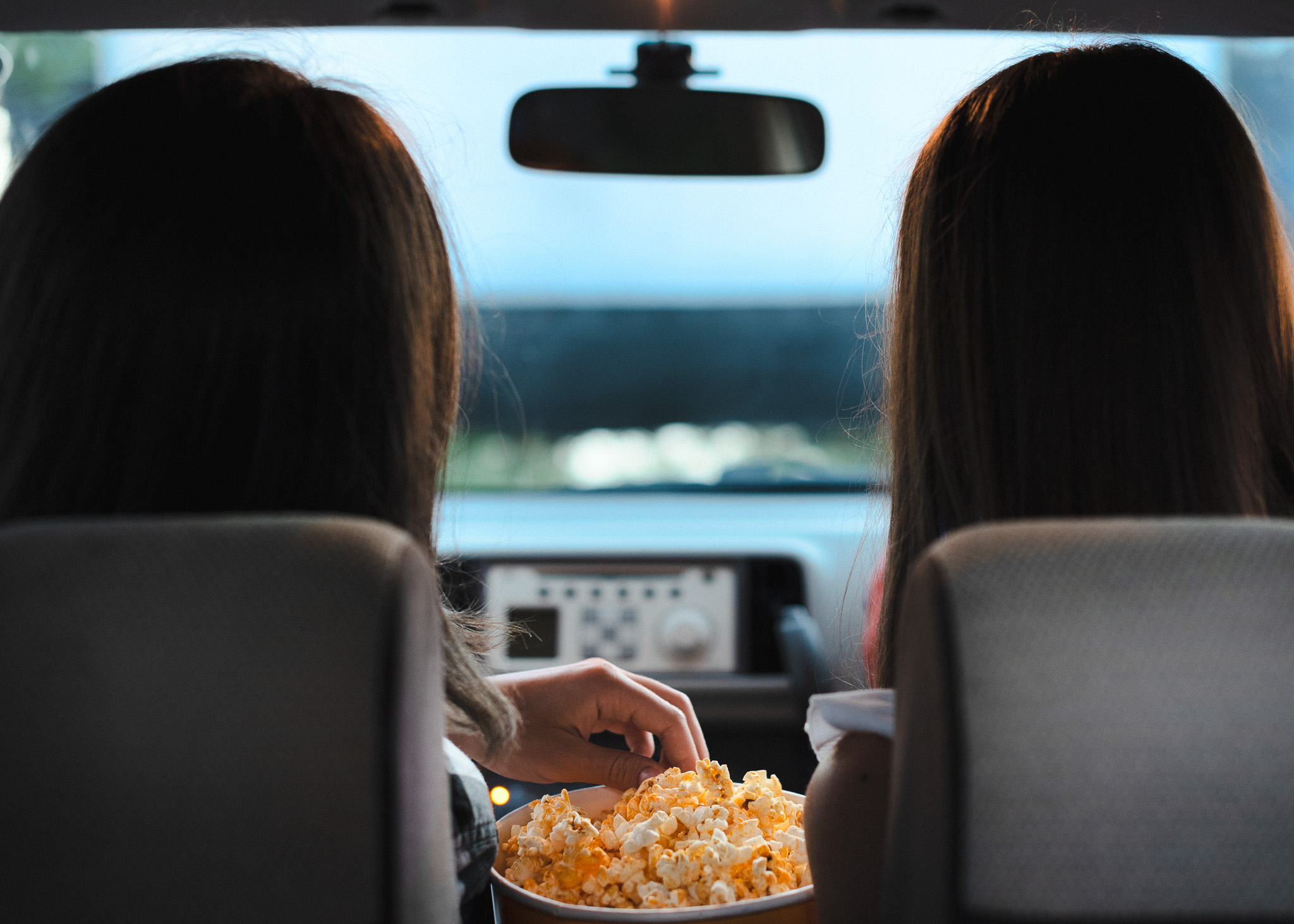 Two people sharing a bucket of popcorn while watching a movie from inside a car at a Maine drive-in theater