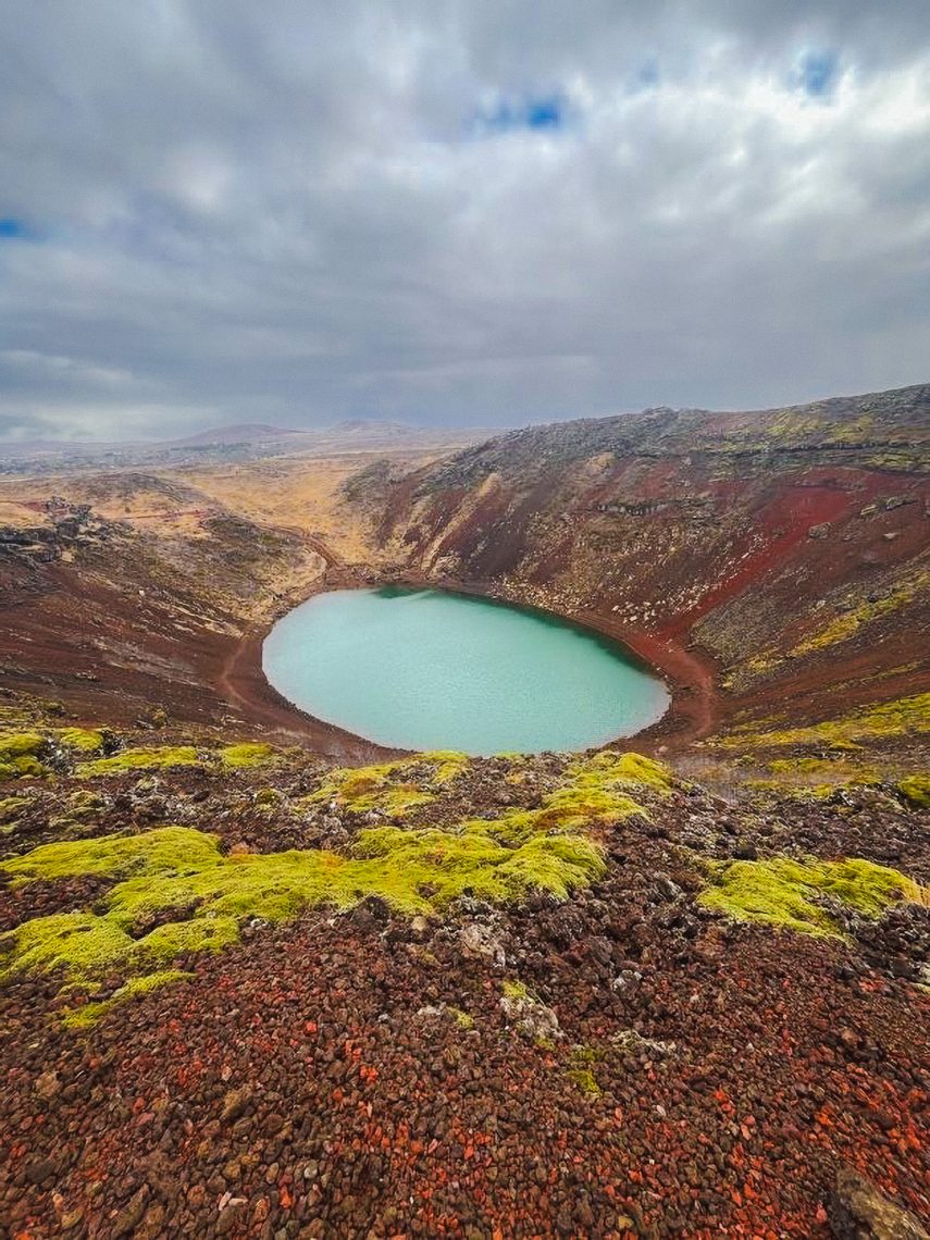 Aerial view of Kerid volcanic crater lake with turquoise water surrounded by red volcanic rock and green moss in Iceland