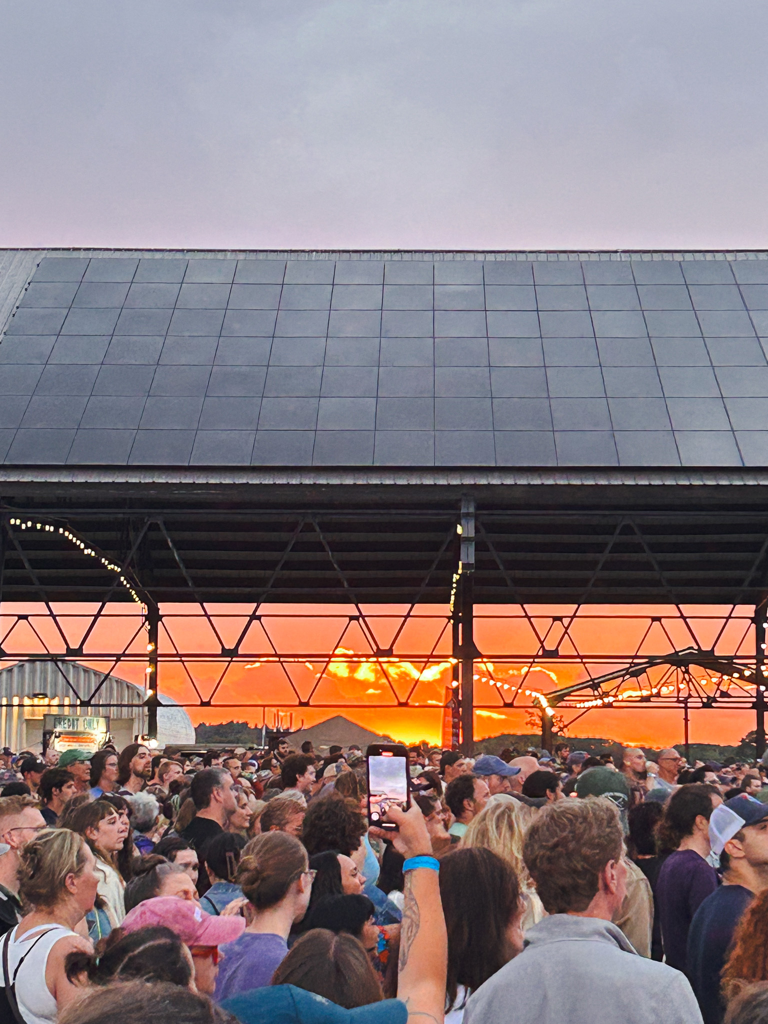 Crowd watching a vibrant orange sunset through the open-air pavilion structure at Thompson's Point in Portland, Maine