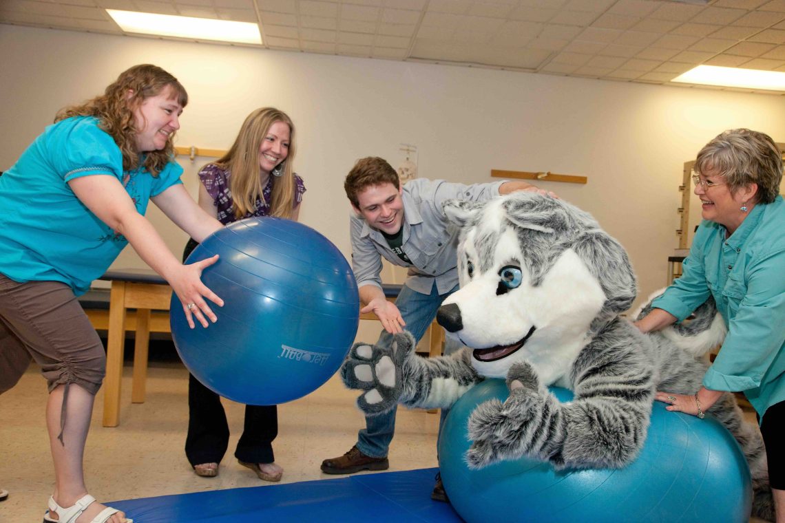 Champ balancing on a therapy ball while cheered on by OT Students and Staff.