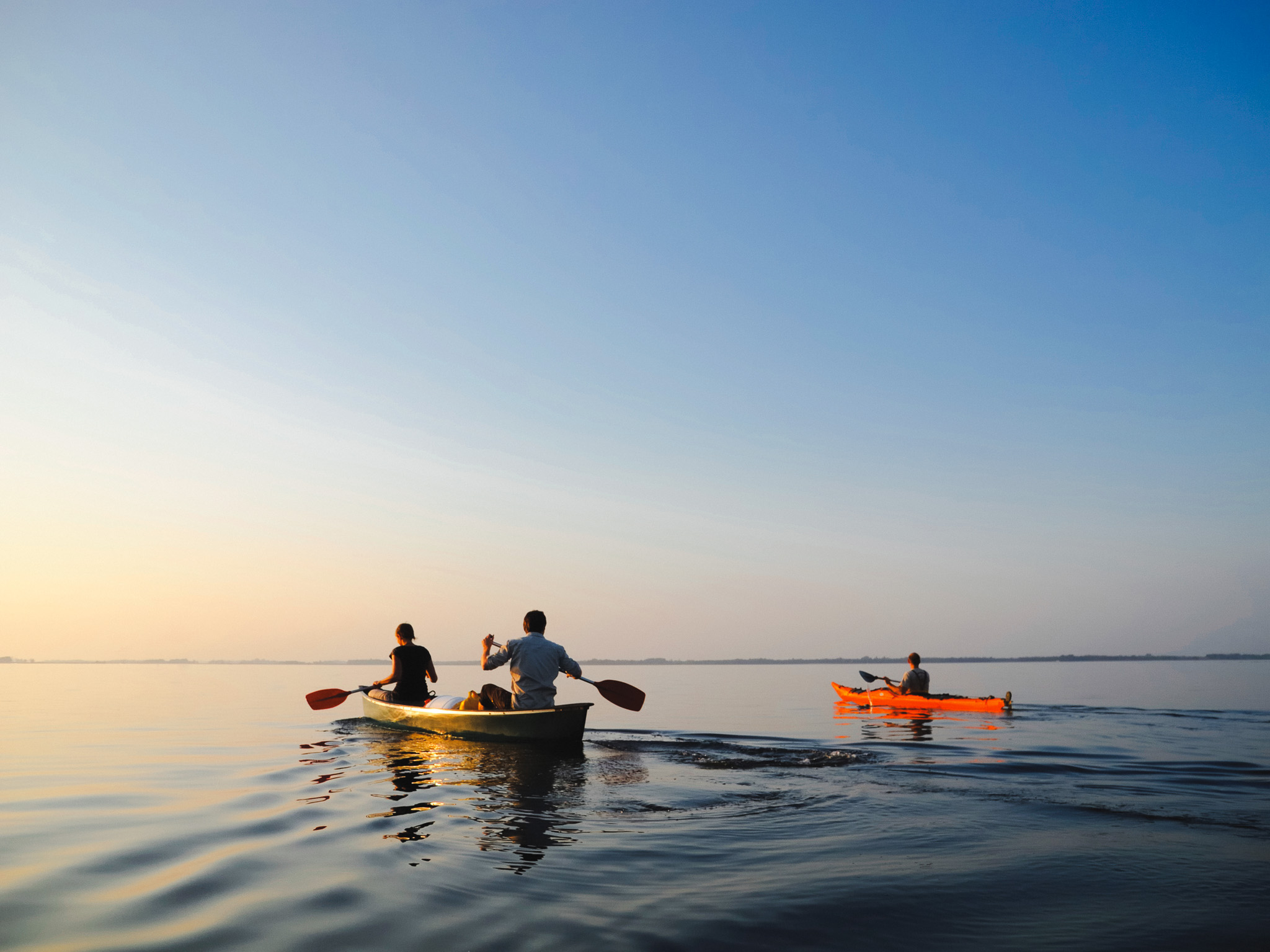 People paddling a canoe and kayak across calm water at sunset in Maine
