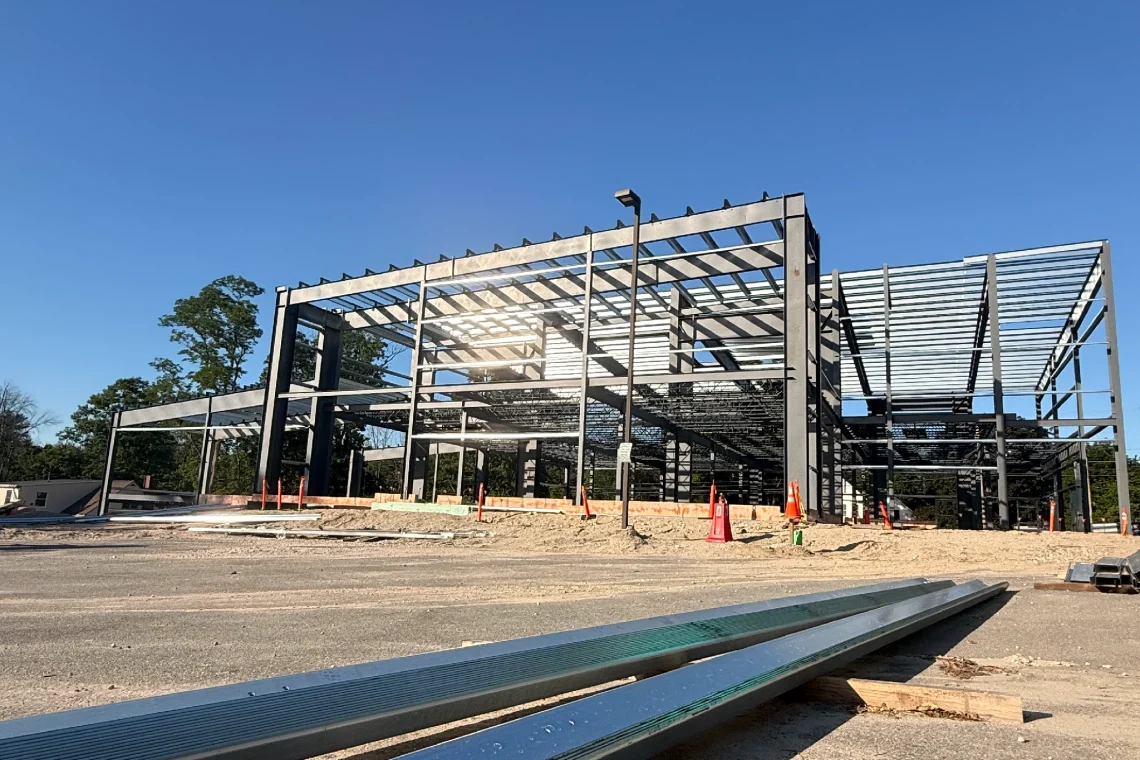 The metal framework of USM's new visual arts building under construction on Gorham campus, with steel beams and structural skeleton visible against a blue sky