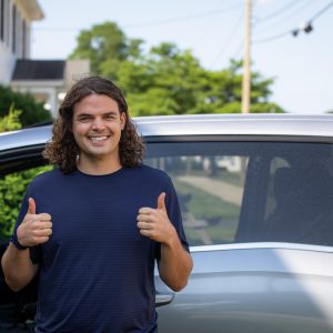 Calvin Soule stands in front of the Green Curtain Roadshow van on departure day, giving two thumbs up and smiling.