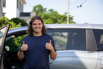 Calvin Soule stands in front of the Green Curtain Roadshow van on departure day, giving two thumbs up and smiling.