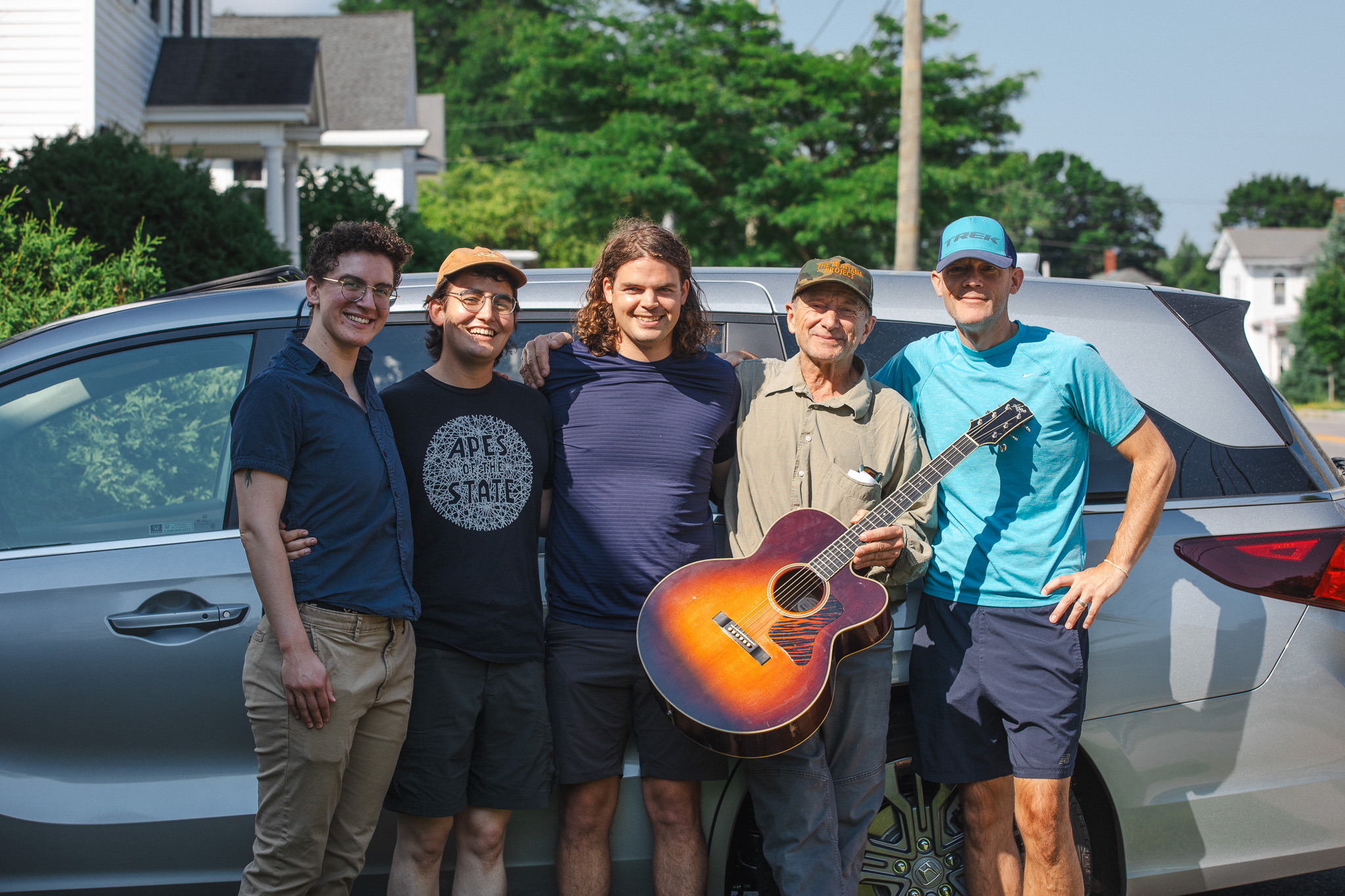 Green Curtain Roadshow participants pose in front of the van on departure day in Portland, Maine. From left to right: an unidentified participant, Eben Thomas, Calvin Soule, Rick Bass holding the Black Ram guitar, and an unidentified participant.