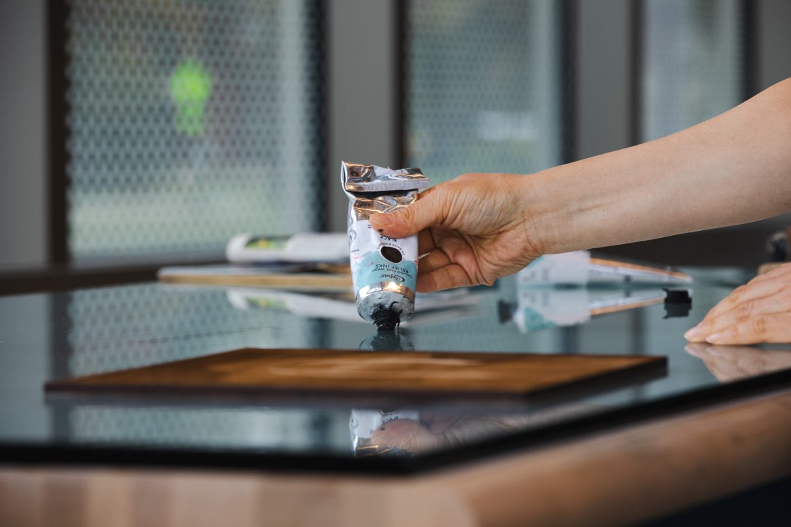 A hand squeezes black relief ink onto a glass inking surface in the Book Arts studio at the Crewe Center.