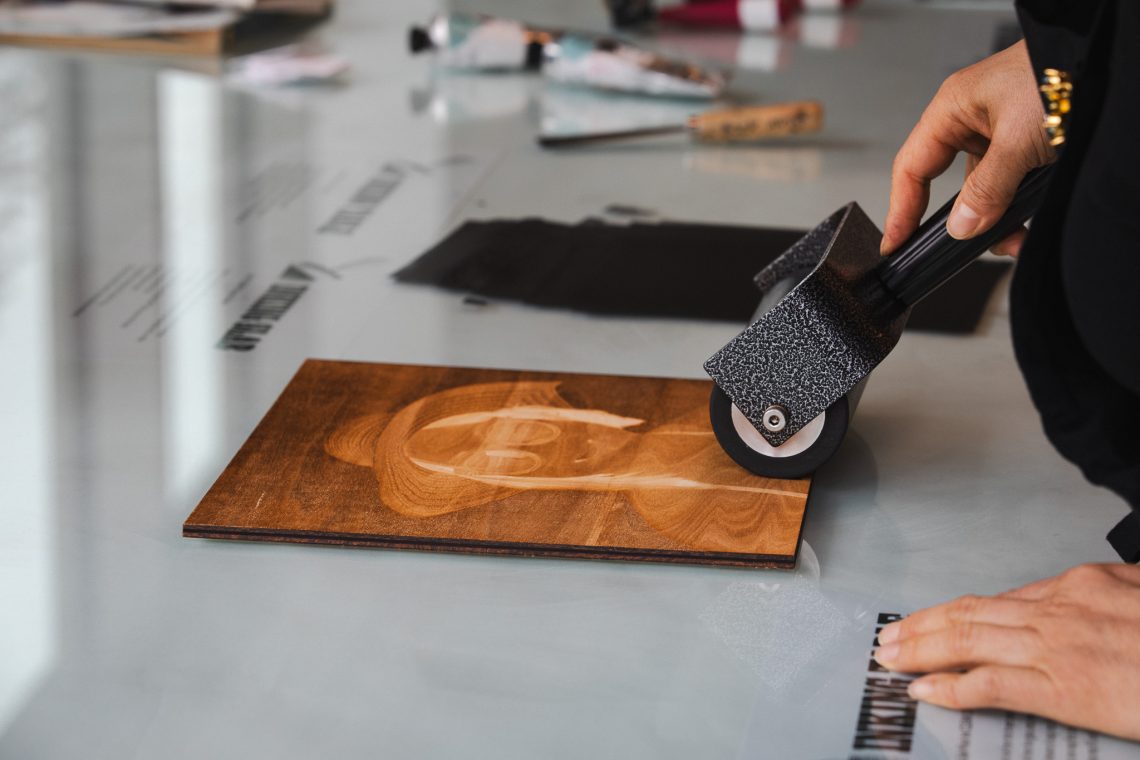 A close-up of hands using a brayer to ink a carved woodblock in the Book Arts studio at the Crewe Center.