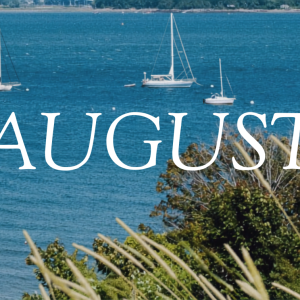 The word "AUGUST" in white text overlaid on sailboats moored in a Maine bay with grasses and trees in the foreground