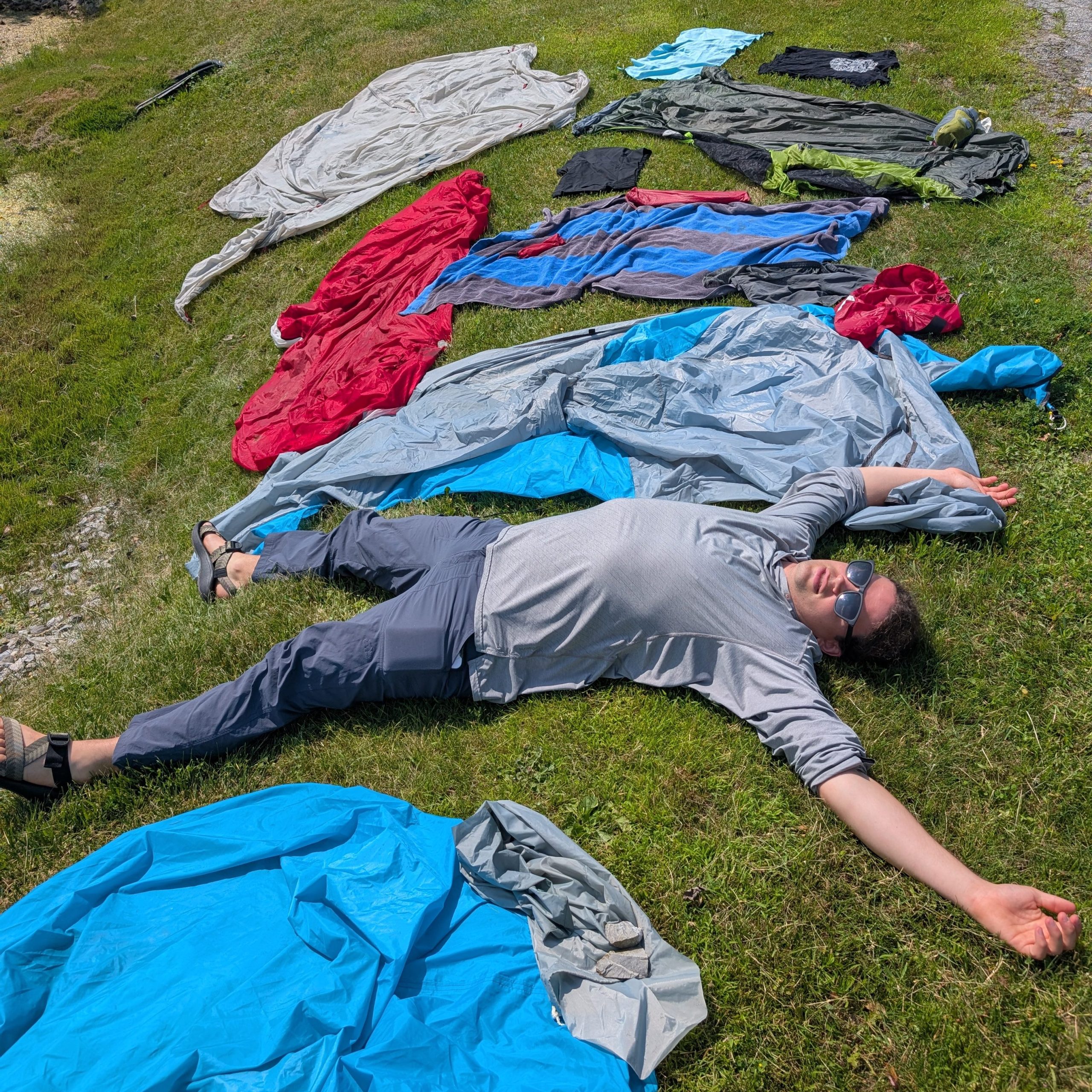 A Green Curtain Roadshow participant lies spread-eagled on a lawn surrounded by tents and camping gear laid out to dry in the sun.