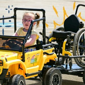 Clare driving in her newly adapted toy car created for her through Go Baby Go and USM.