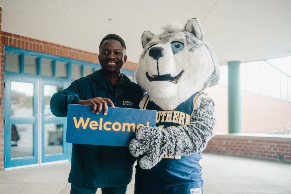 A student holding a "Welcome" sign next to Champ.