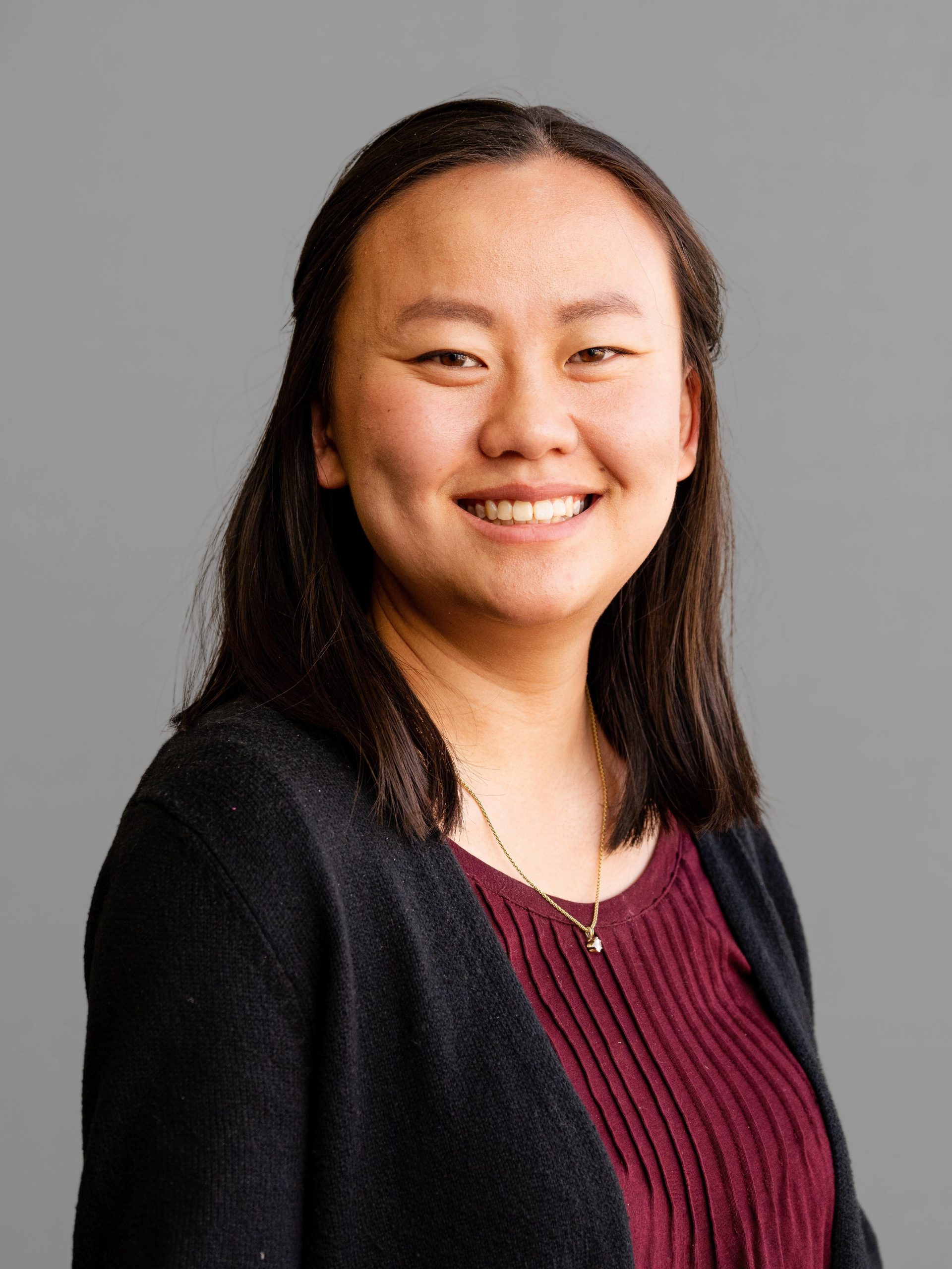 Maya Twombly, MIST Lab Manager, smiles at the camera in a professional headshot against a gray background. She wears a burgundy top and black cardigan.