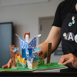 Annie Lee-Zimerle holds open a colorful pop-up artist book featuring a three-dimensional garden scene.