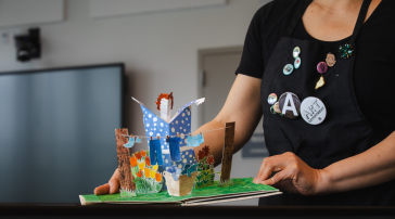 Annie Lee-Zimerle holds open a colorful pop-up artist book featuring a three-dimensional garden scene.