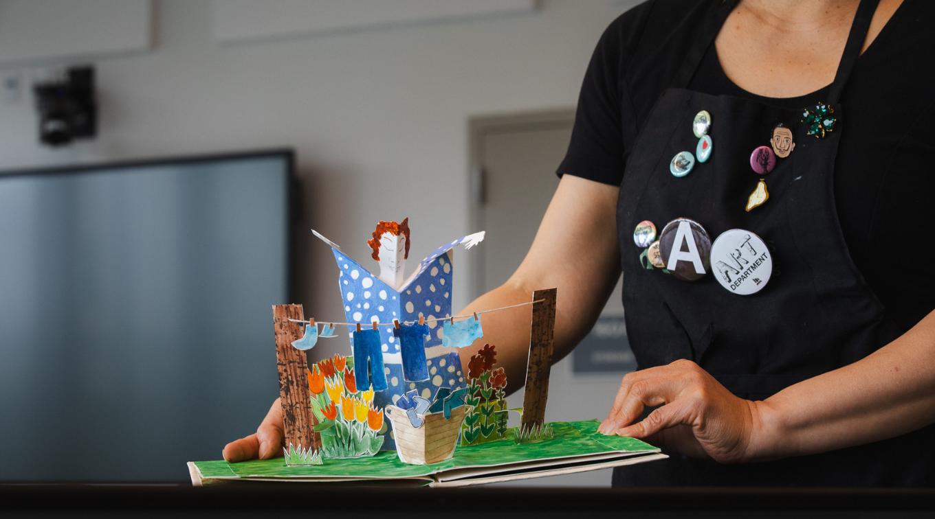 Annie Lee-Zimerle holds open a colorful pop-up artist book featuring a three-dimensional garden scene.