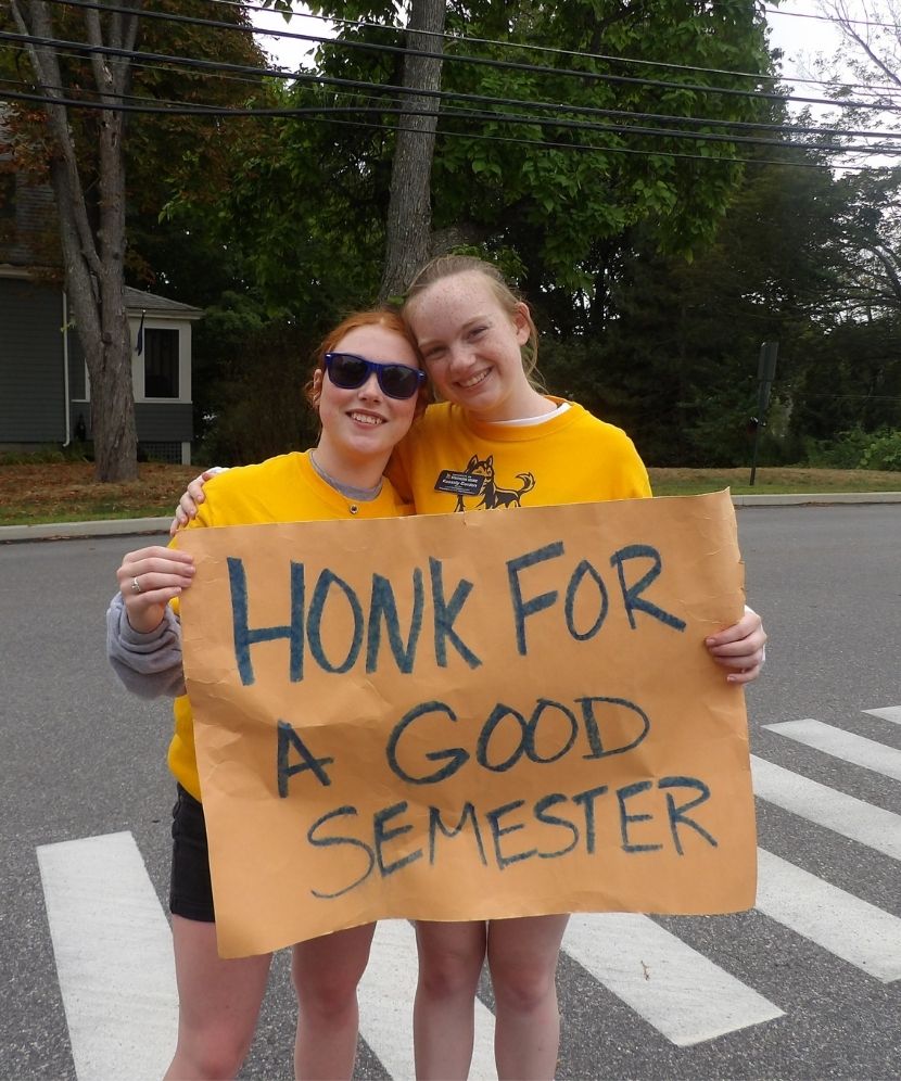 Two husky mentors holding a sign that says "Honk for a good semester".