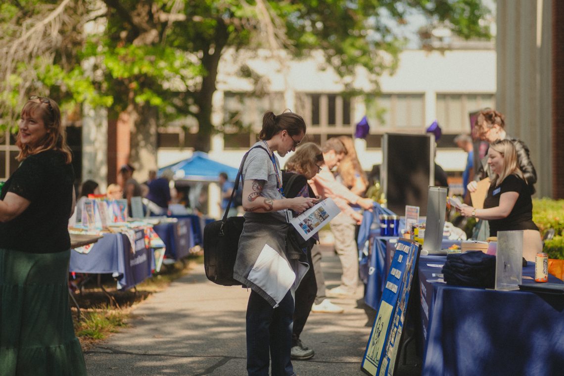 Students browse a row of club and organization tables lining a campus walkway during an outdoor fair.