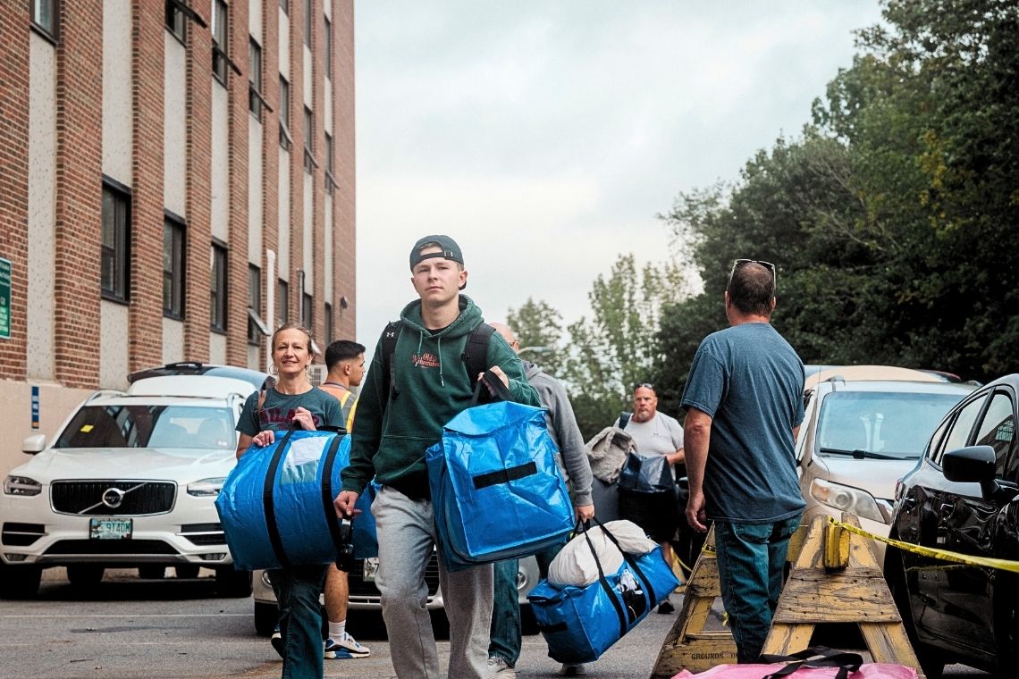 A student with parents, arms full of tote bags moving into a dorm on Gorham campus.